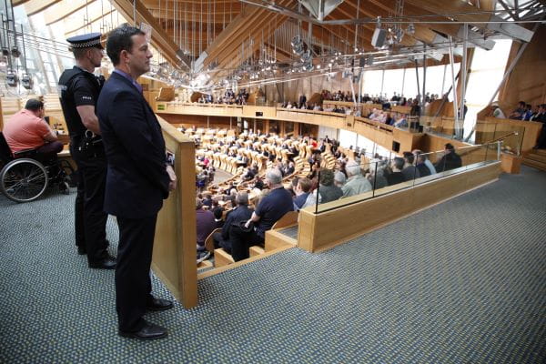 the viewing area of the public gallery with security staff looking on at visitors in rows of seats