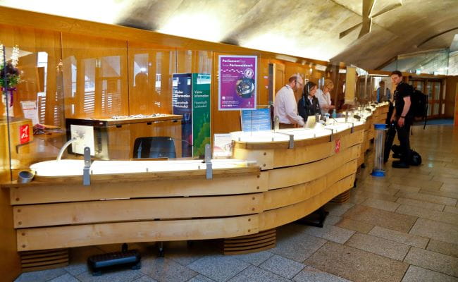 parliament staff stand behind the visitor info desk while a visitor stands in front them