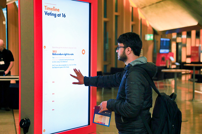 a visitor touches the interactive touchscreen exhibit in the main hall