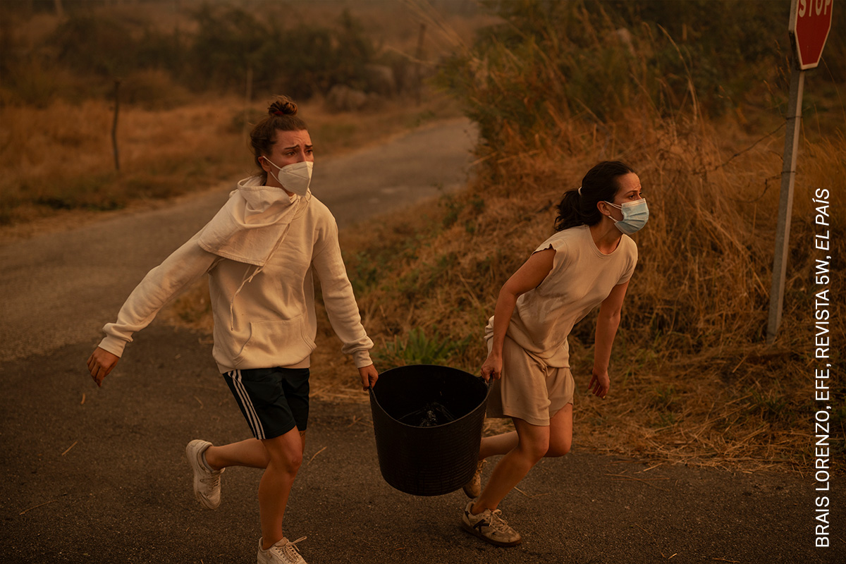 Two women run with a bucket of water to help fight a wildfire in Carballeda de Avia, Ourense, Galicia, Spain.