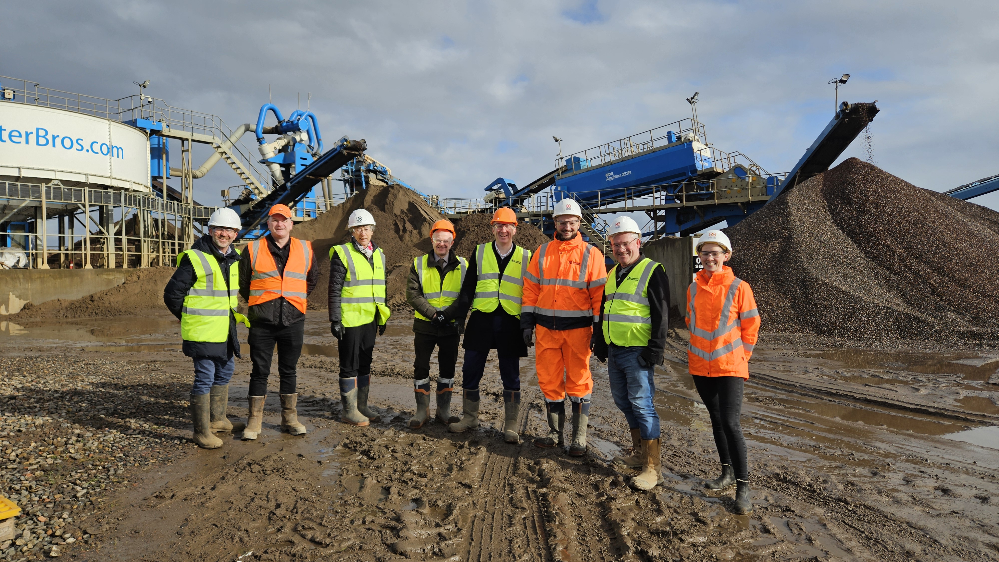Photograph of four Finance and Public Administration Committee Members stood, with staff from Brewster Brothers, in front of machinery during the fact-finding visit