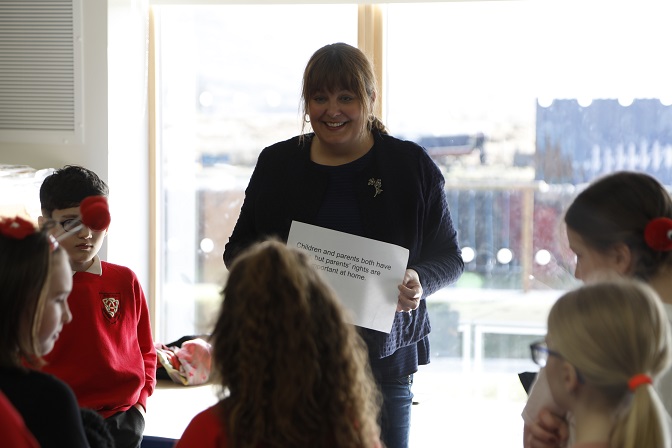 Ruth Maguire is holding a sign which reads children and parents both have rights but parents' rights are more important at home. She is surrounded by students.